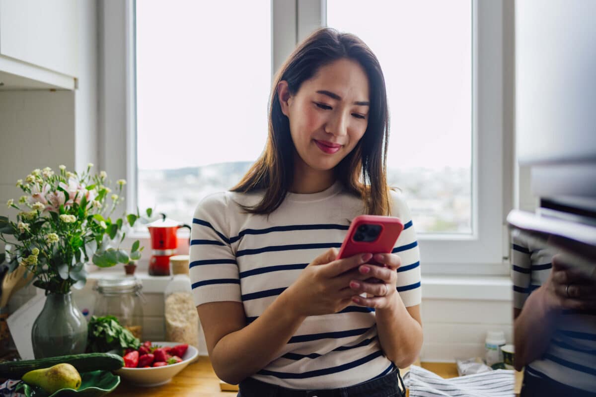 Woman in kitchen looking at phone & smiling