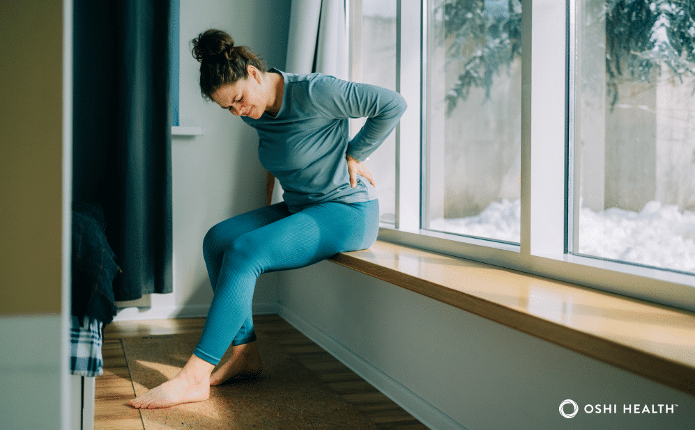 Person sitting on a window ledge and holding their lower back, illustrating lower back pain that may be associated with constipation.