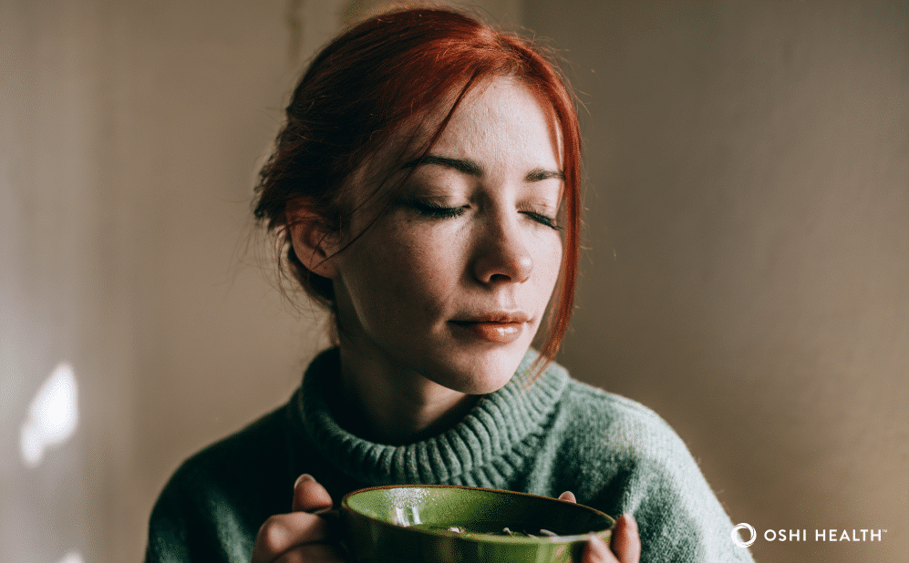 A woman with red hair holds a green bowl near her face with her eyes closed, representing the experience of an IBS flare-up.
